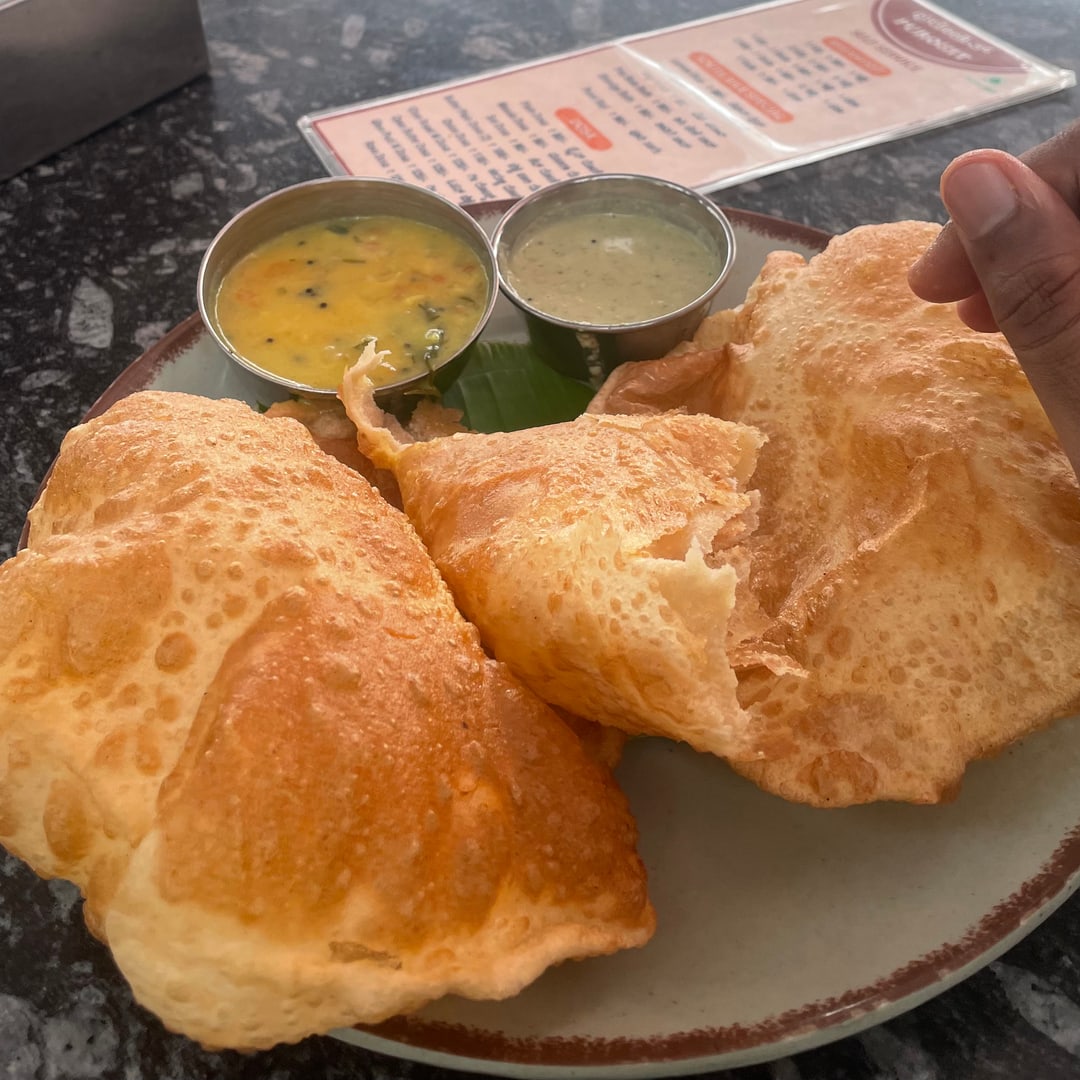 A plate of poori photographed on a phone at a cafe table